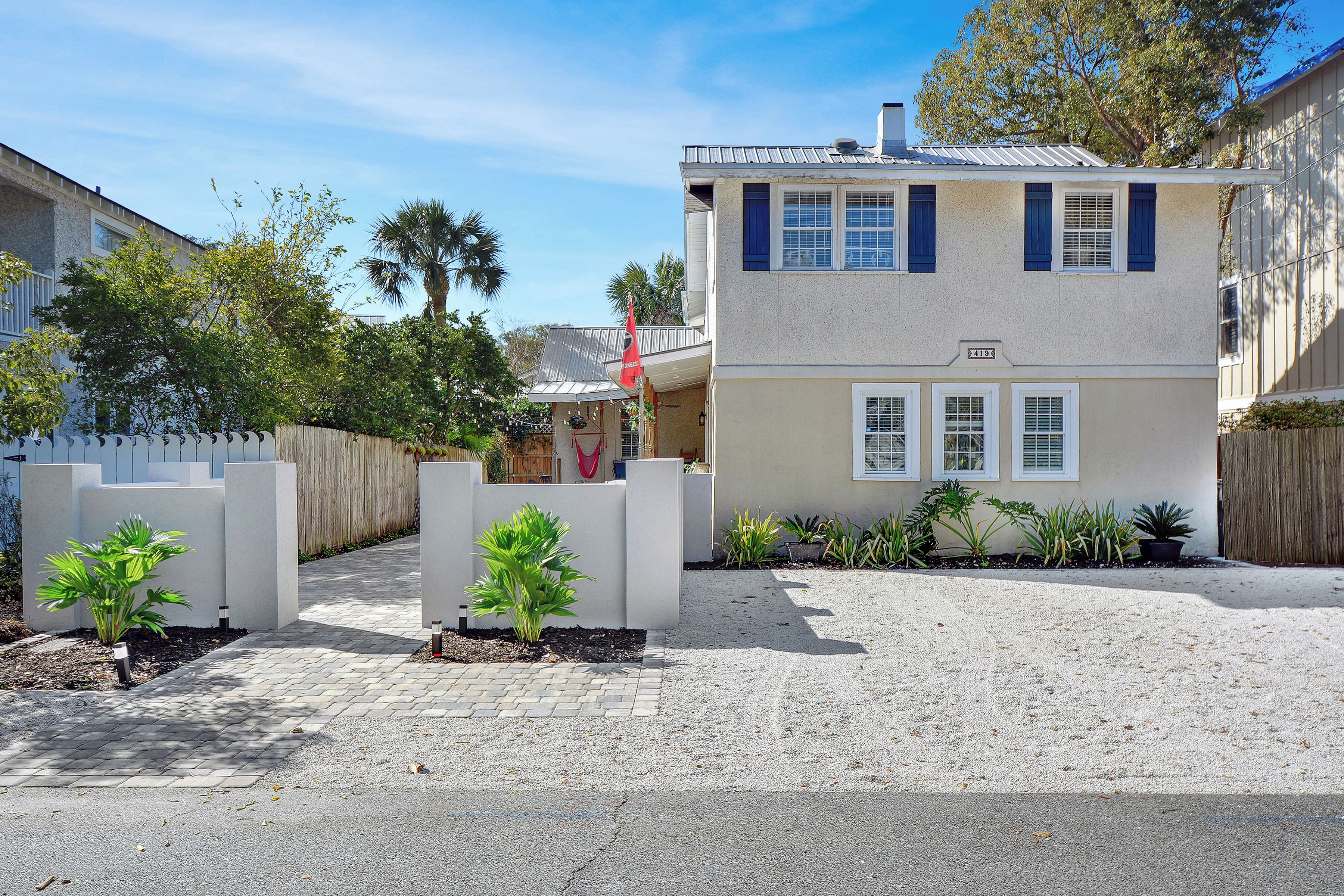 A two-story house with a paved driveway and a small garden area with potted plants.