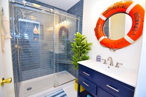 A bathroom with a glass shower enclosure, a blue tiled wall, a white sink with a blue cabinet, and a life ring on the wall. - Twin Tree Road 511 3 Bedroom Home by RedAwning (Ocean City)