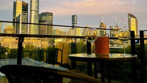 A cityscape view from a balcony with modern buildings, a glass table, and a wicker basket. - Charming Urban Retreat (South Brisbane)