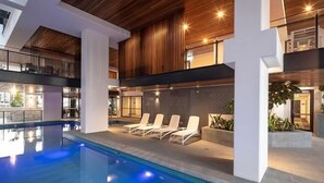 A modern indoor pool area with lounge chairs, a wooden ceiling, and a view of the bar area. - Charming Urban Retreat (South Brisbane)
