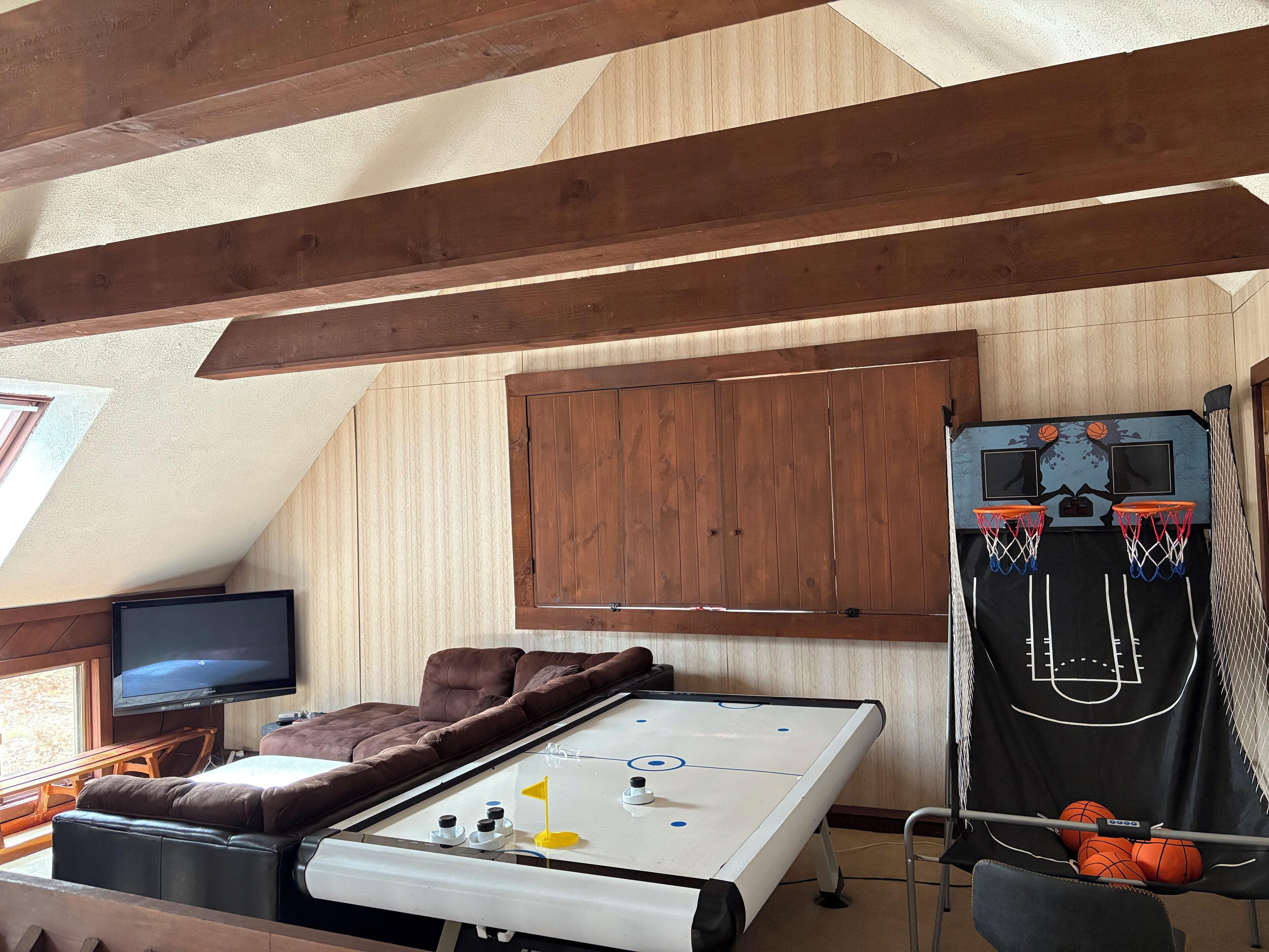 Una habitación con ventilador de techo, televisión, sofá, una mesa con un disco de hockey y un aro de baloncesto.