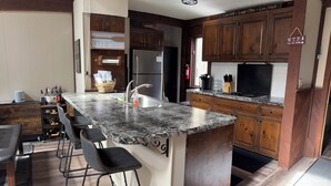 A kitchen with a granite countertop, wooden cabinets, and a bar area with stools.