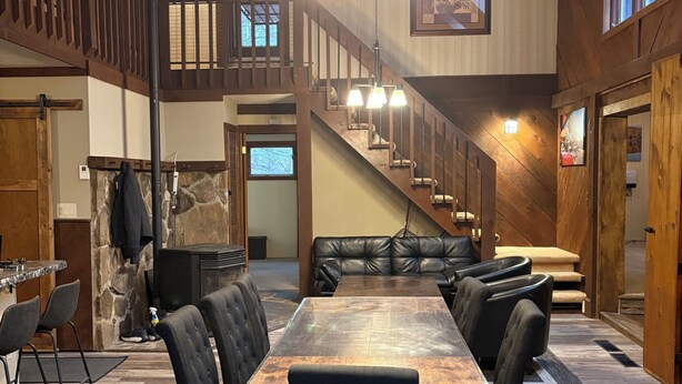 A spacious dining area with a long table and multiple chairs, a staircase, and a stone wall.