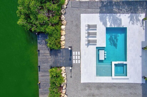 An aerial view of a modern pool area with a wooden deck, a stone border, and a clear blue pool.