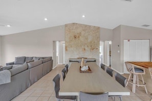 Un comedor moderno con una mesa larga, sofá gris y una pared decorativa.