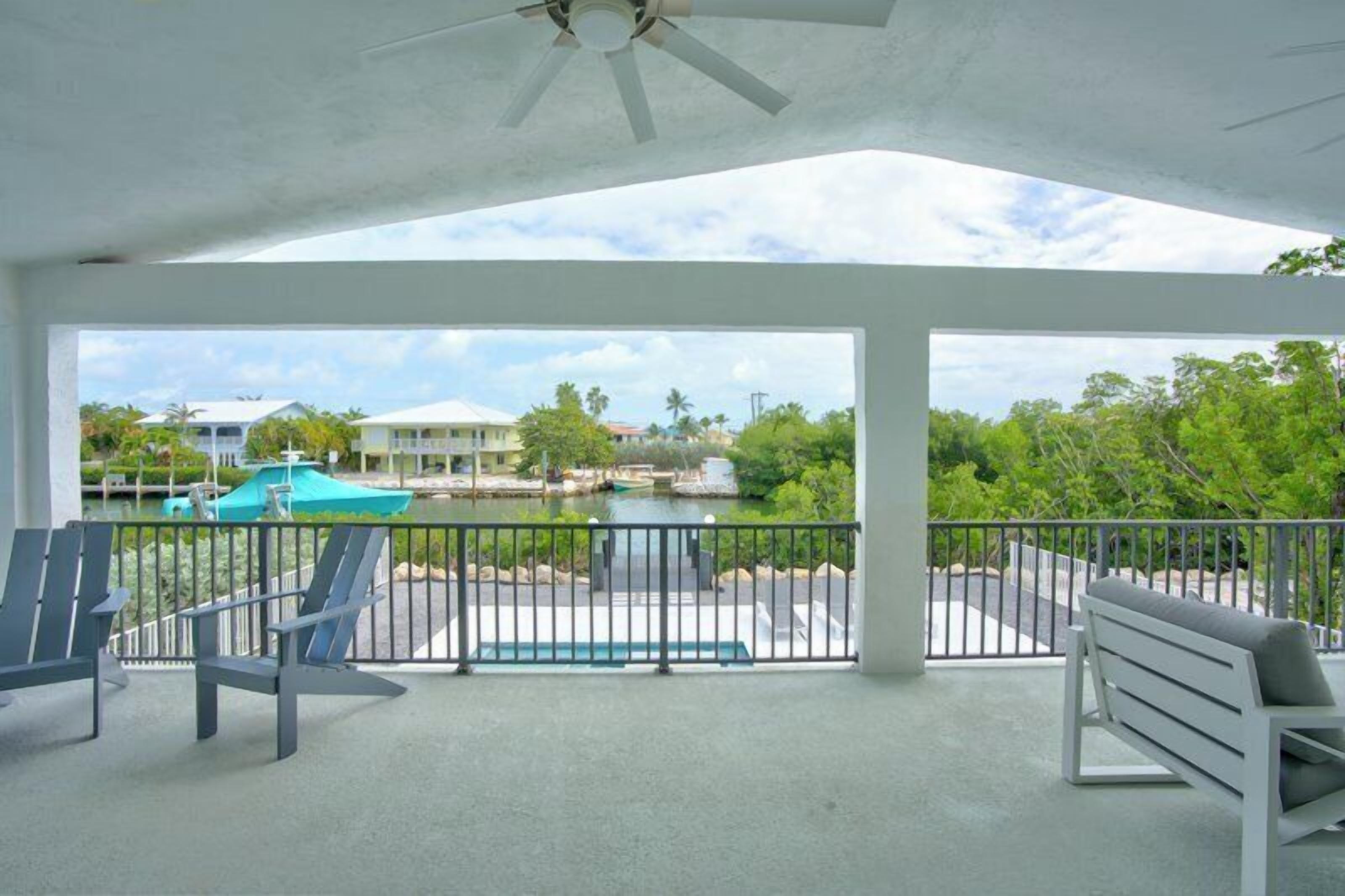 A covered balcony with a view of a marina, a pool, and surrounding greenery.