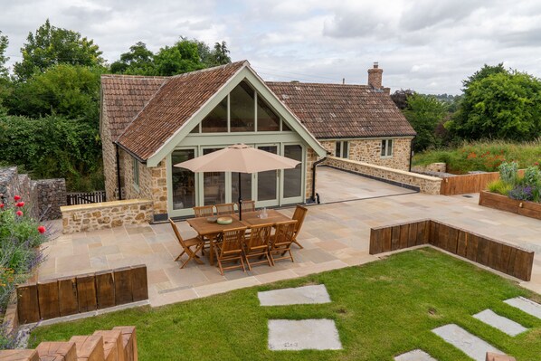 Une maison en pierre avec un toit en tuiles et une terrasse équipée d’une table et de chaises.