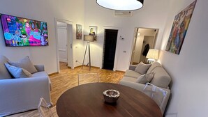 A modern living room with a round wooden table, clear plastic chairs, a large flat-screen TV, and a black pendant light. - Newly renovated, located on the 2nd floor in a very quiet area of Trastevere. (Roma)