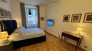 A hotel room with a bed, a desk, a TV, and framed pictures on the wall. - Newly renovated, located on the 2nd floor in a very quiet area of Trastevere. (Roma)