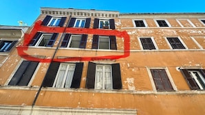 A multi-story building with a yellow facade, multiple windows with shutters, and a stone base. - Newly renovated, located on the 2nd floor in a very quiet area of Trastevere. (Roma)