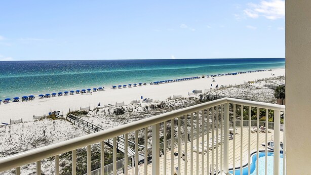 Blick auf einen Strand vom Balkon aus, mit Pool und Strandstühlen.