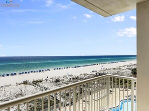 Une vue sur la plage depuis un balcon, avec une piscine et des parasols de plage.