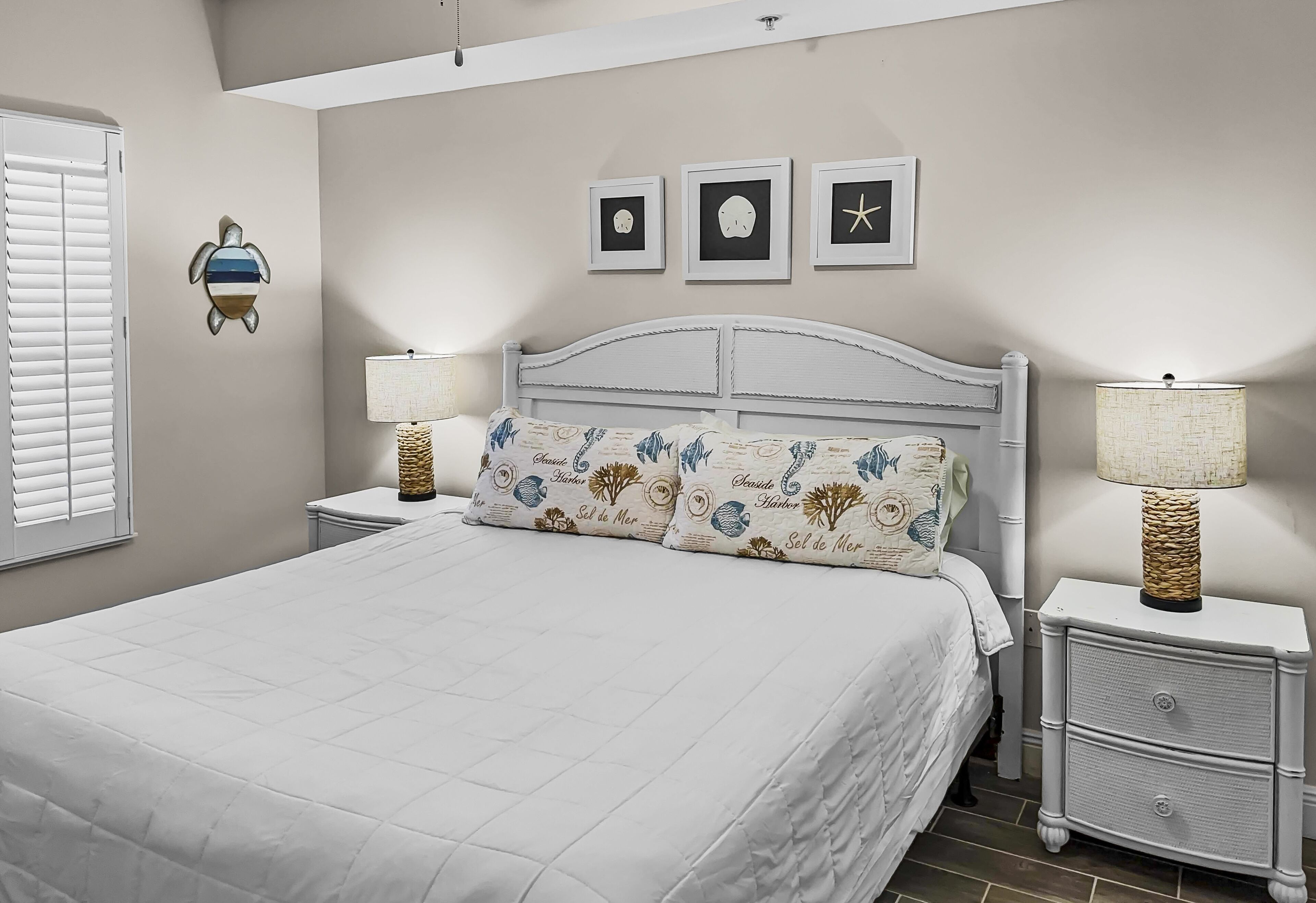 Un dormitorio con una cama, dos mesitas de noche, una mesilla auxiliar, un estante en la pared y una ventana con persianas.