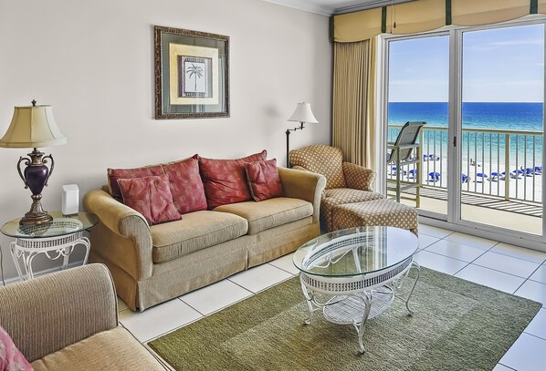 A living room with a beige sofa, a patterned armchair, a glass coffee table, and a view of the beach through large glass doors. - SMP 502 | 3Bd Gulf Front Condo | Free Seasonal Beach Service | All King Beds! (Fort Walton Beach)