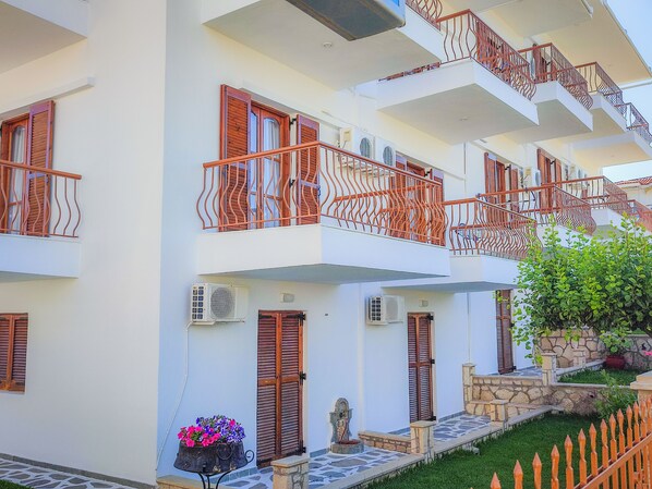 Un edificio de varios pisos con balcones, unidades de aire acondicionado y un pequeño jardín.