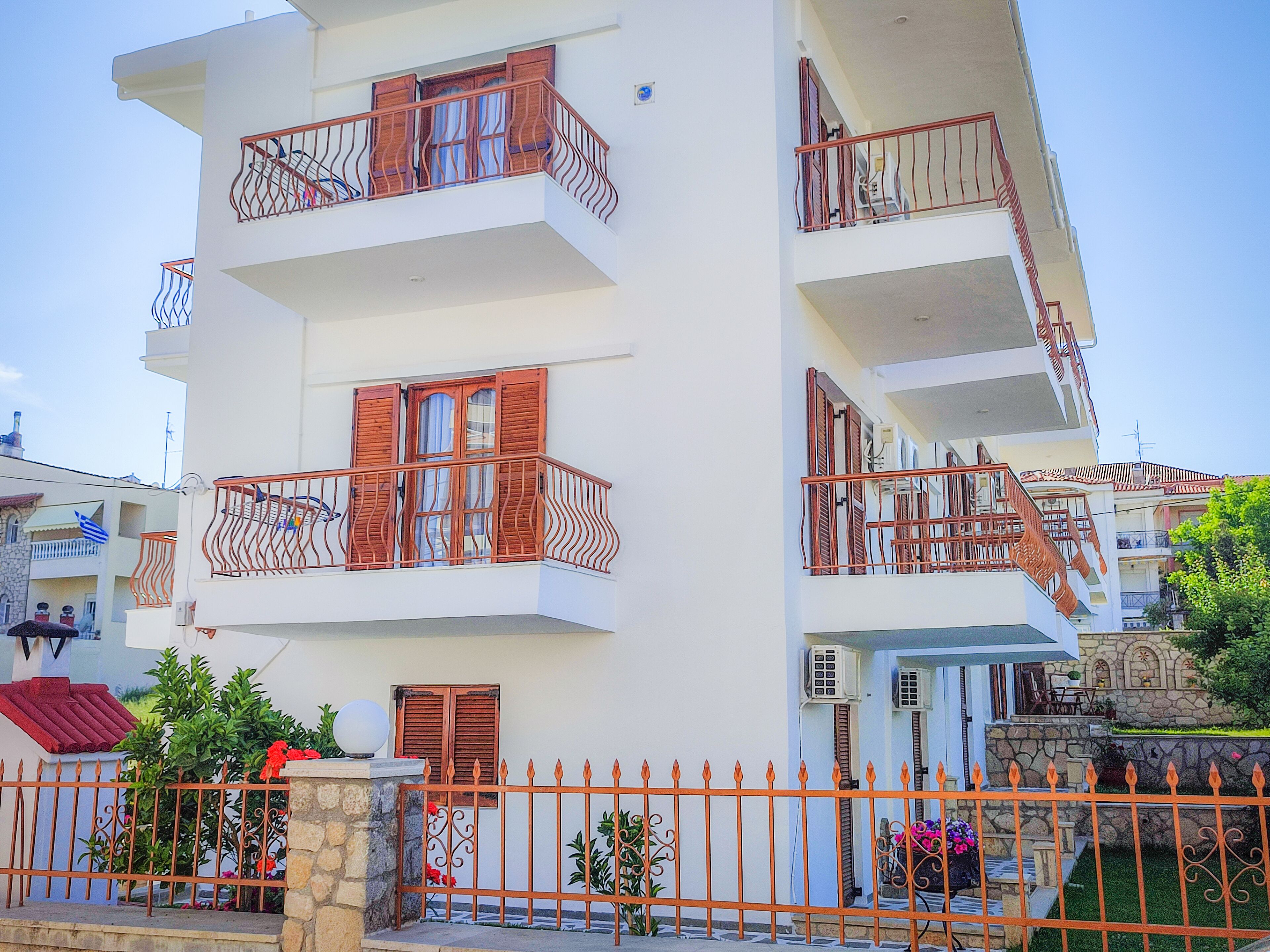 A multi-story residential building with balconies, a stone base, and a metal fence.