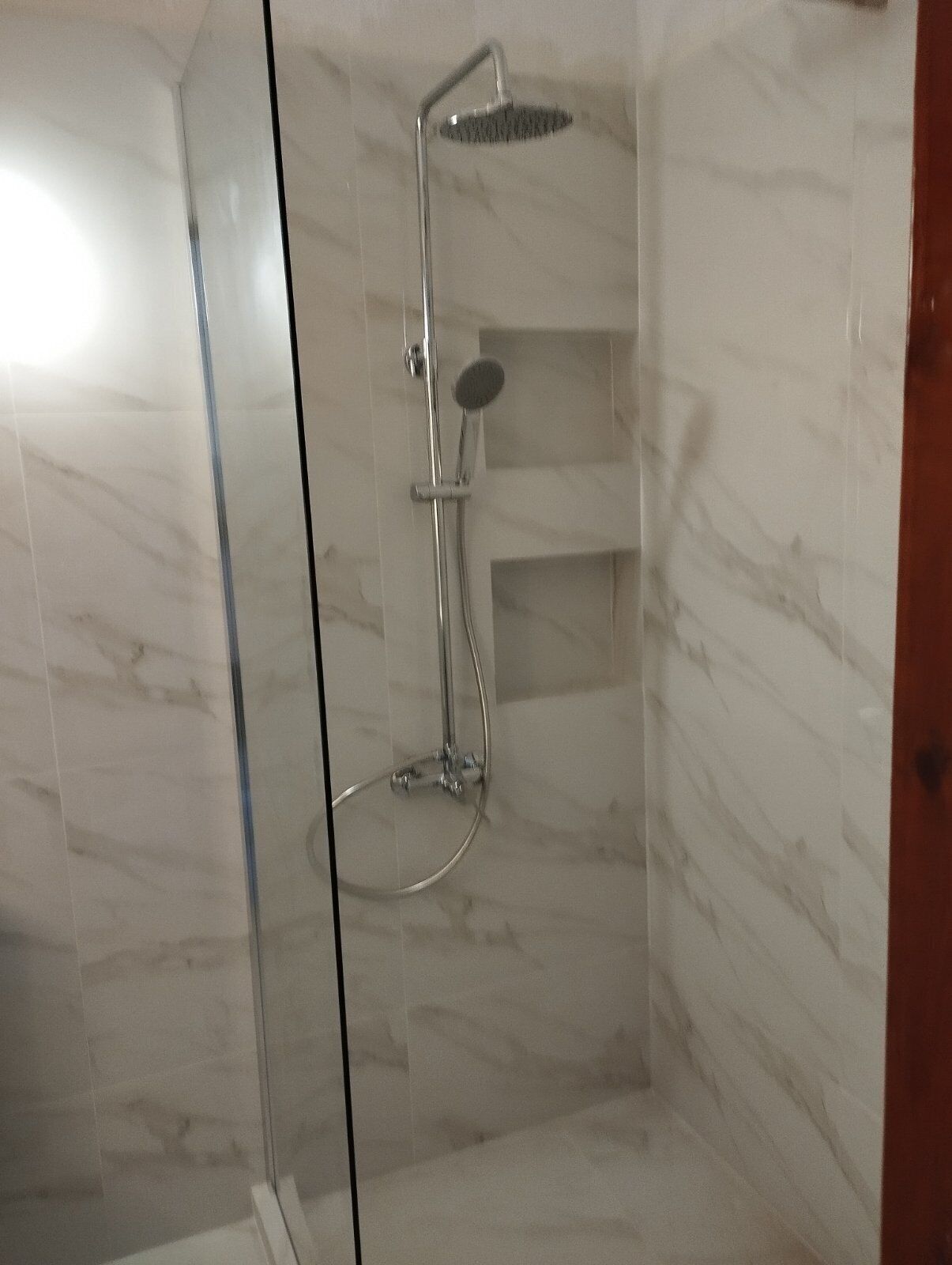 Une douche fermée par des parois en verre, dotée d’un pommeau de douche à main et d’un robinet mural.