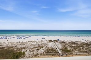 A beach with white sand, a clear blue sky, and a wooden boardwalk leading to the water.