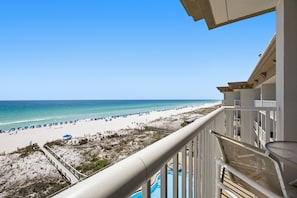 A balcony with a view of a beach, a pool, and a clear blue sky.