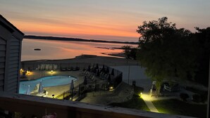 Zona de piscina con sillas de descanso y sombrillas, con vista a una masa de agua tranquila al atardecer.