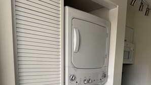 Un lavadero compacto con lavadora y secadora de carga frontal, un microondas y un mueble pequeño.