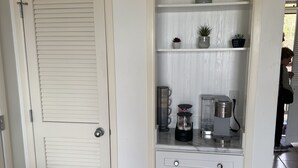 Una puerta blanca con manija, un armario blanco con cajones y una encimera con una cafetera y una planta.