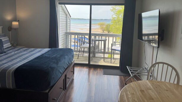 Un dormitorio con cama, televisión, balcón con mesa y sillas, y vista a la playa.