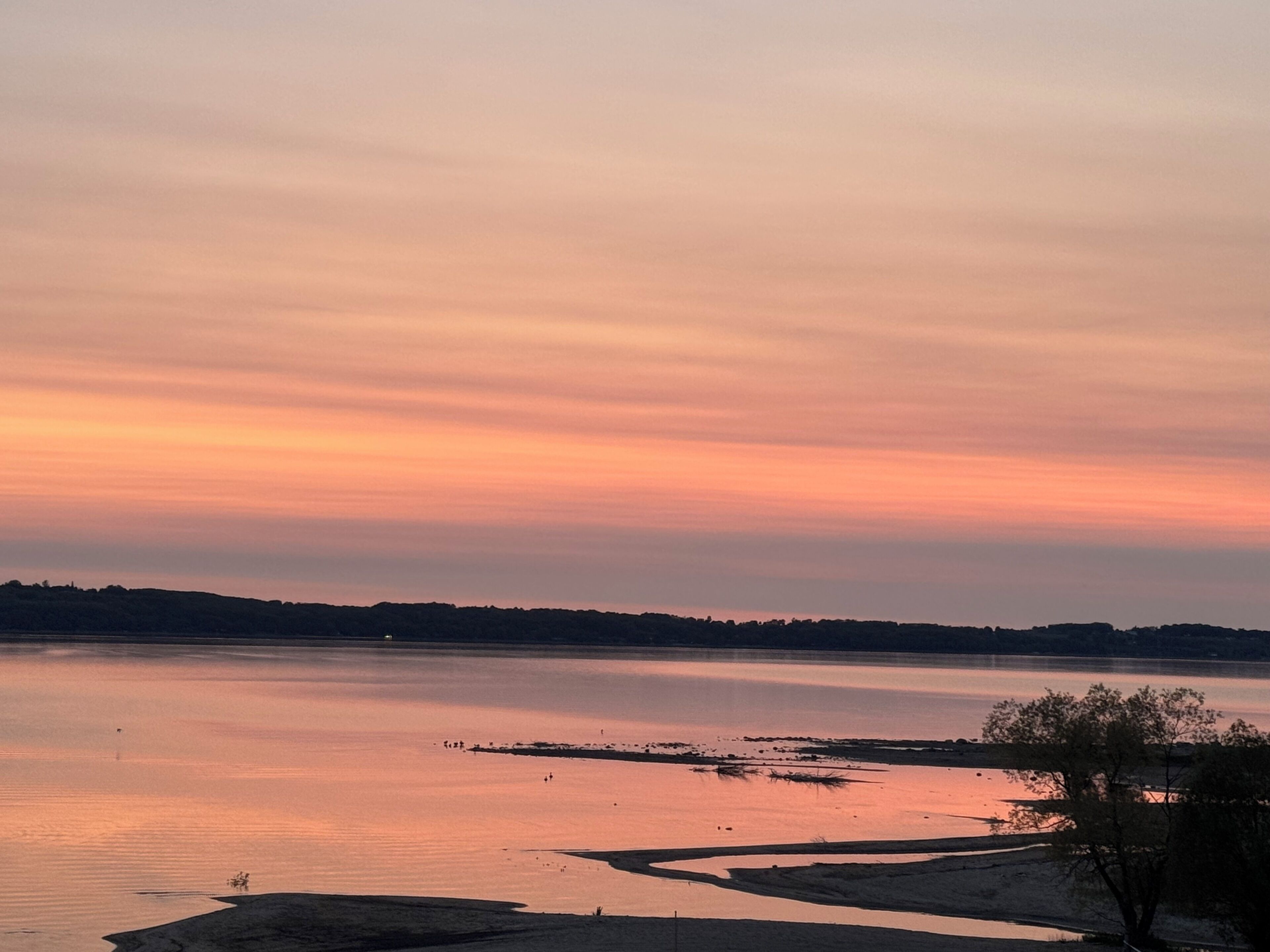 Tyyni järvi auringonlaskun aikaan, ja kauempana näkyy rantaviiva.