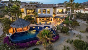 Une maison luxueuse dotée d’une piscine, d’un espace extérieur aménagé et d’une structure surmontée d’un toit de chaume.