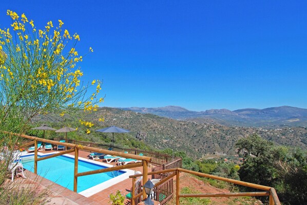 A pool area with a wooden deck, lounge chairs, and umbrellas, overlooking a mountainous landscape. - Amazing villa. Impressive views. (Comares)