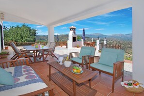 Une terrasse avec des meubles en bois, une table garnie de fruits et une vue sur les montagnes.