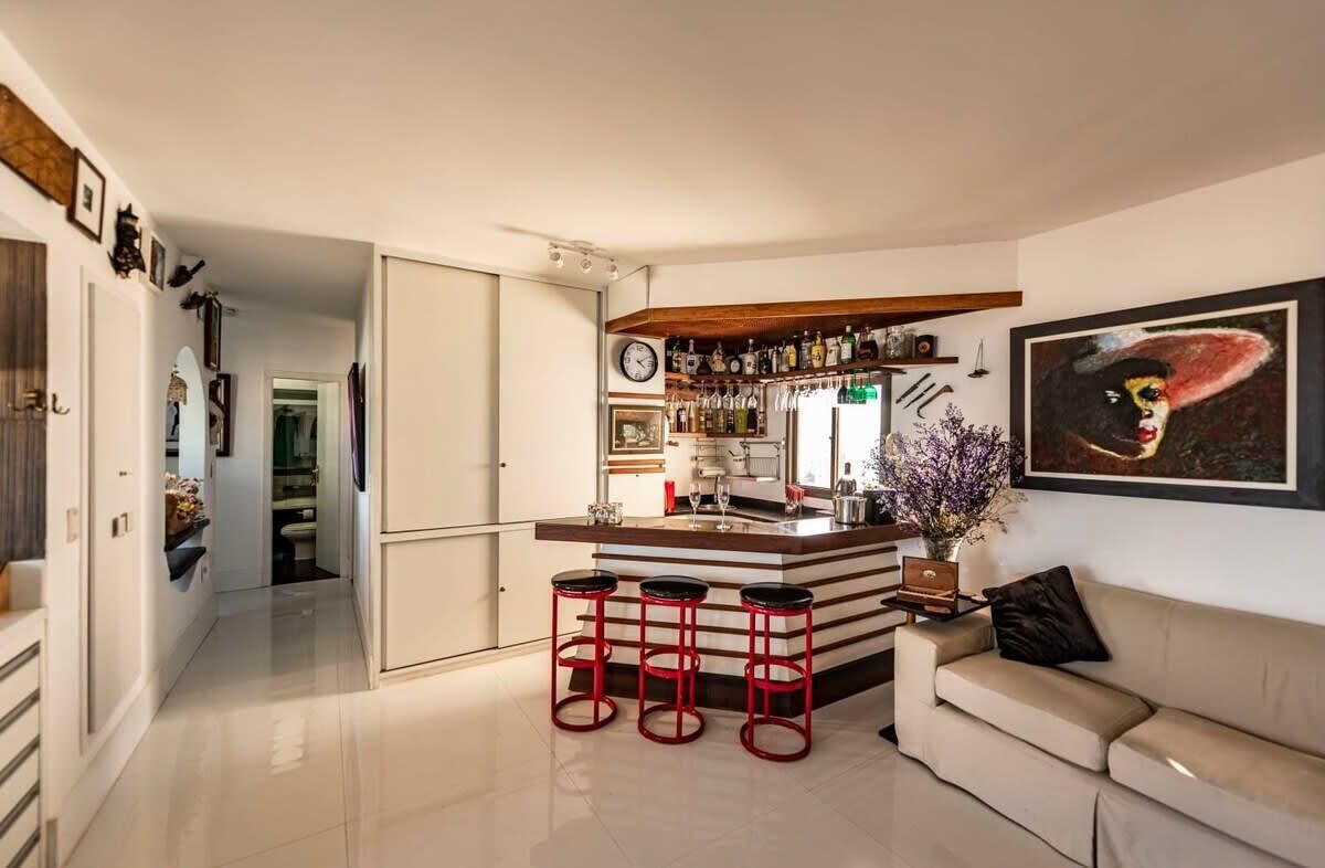 Una cocina moderna con barra, taburetes rojos y un cuadro grande en la pared.