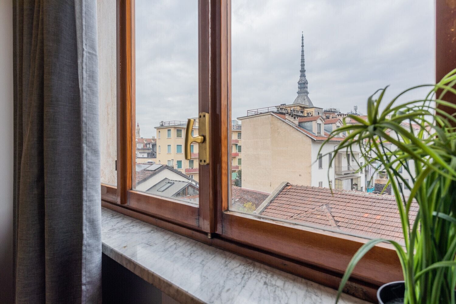 A window with a view of a building with a tall spire, a potted plant, and a curtain.