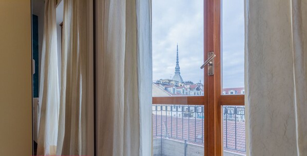 A room with a large window, curtains, and a view of a cityscape with a tall building.