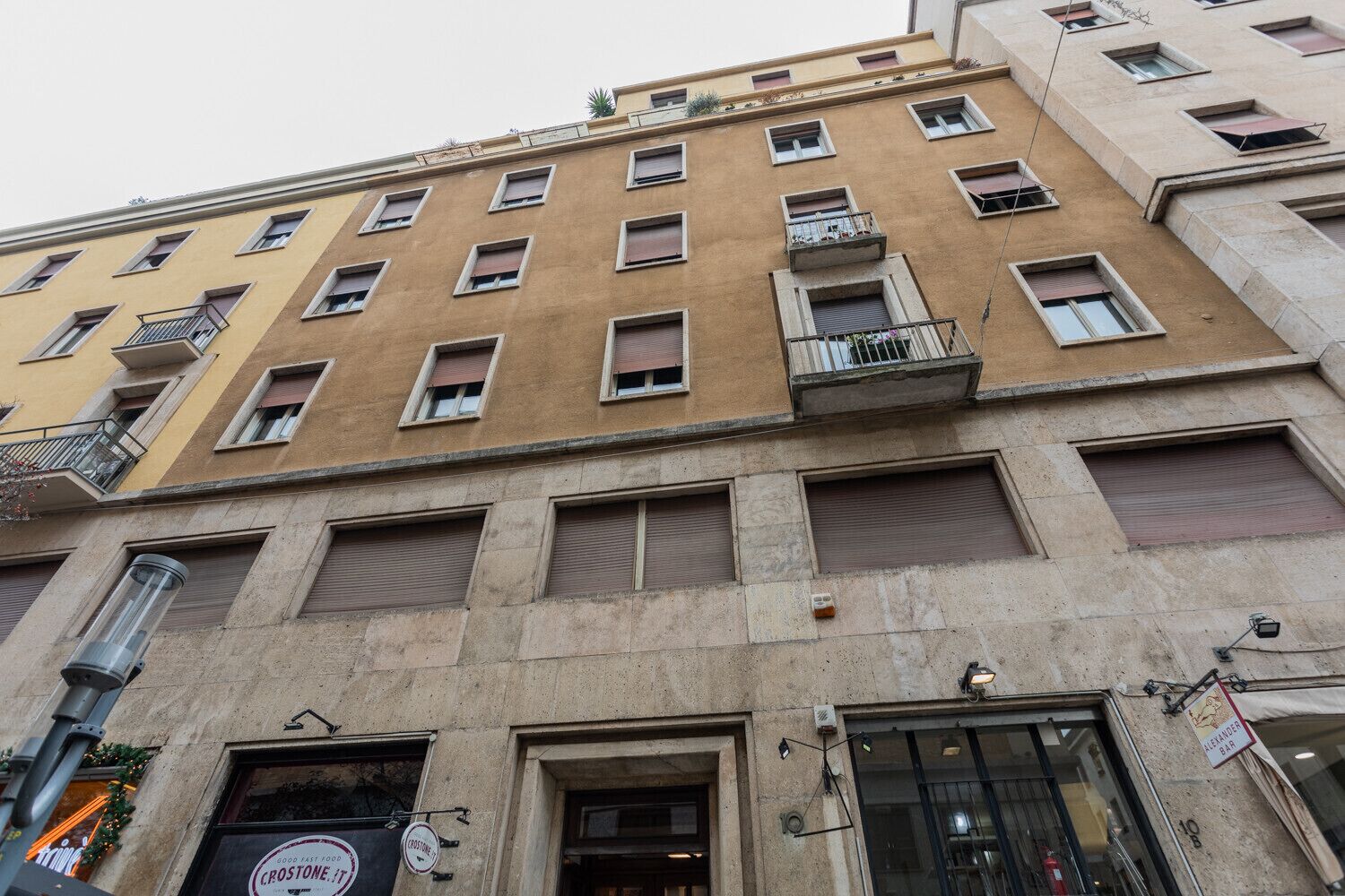 A multi-story building with a beige facade, multiple balconies, and a ground-level entrance with a sign for 'Crostone IT'.