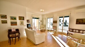 A spacious living room with wooden flooring, a white sofa, a dining table with chairs, and several paintings on the walls. - Panorama Apt in Ospedaletti by Wonderful Italy (Ospedaletti)