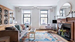 Un salon comprenant un canapé, un fauteuil, un meuble en bois, une cheminée et un tapis à motifs.