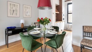 Un coin repas avec une table en verre, des chaises vertes, un luminaire suspendu rouge et des œuvres d’art accrochées au mur.