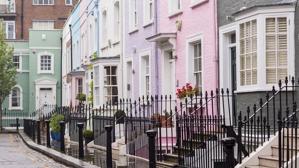Une rangée de maisons colorées à étages, dotées de balcons en fer forgé noir et bordant une rue pavée.