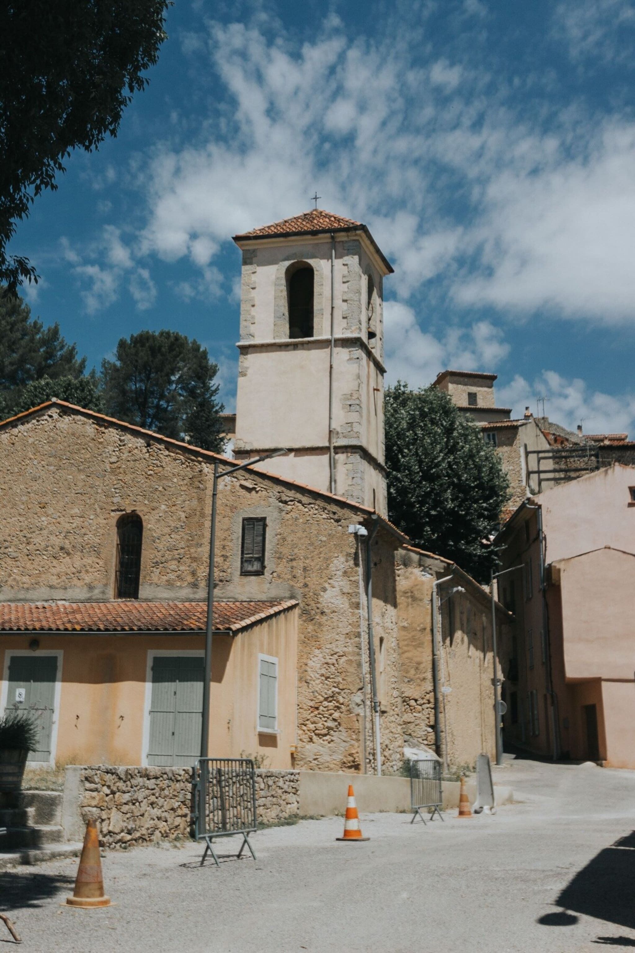 A historic building with a bell tower, stone walls, and a paved street with traffic cones.