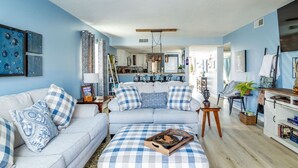 A living room with a sofa, ottoman, and a coffee table. There is a kitchen in the background. - Just steps from your private patio to the river (Townsend)