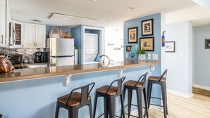 A modern kitchen with a central island, bar stools, and a dining area. - Just steps from your private patio to the river (Townsend)