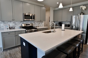 A modern kitchen with grey cabinets, stainless steel appliances, a large island with bar stools, and pendant lighting. - Small Dogs Allowed (up to 40 pounds total) * New Bayside Resort (Selbyville)