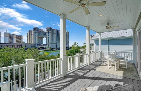 A covered outdoor area with a white railing, a ceiling fan, and a table with chairs.