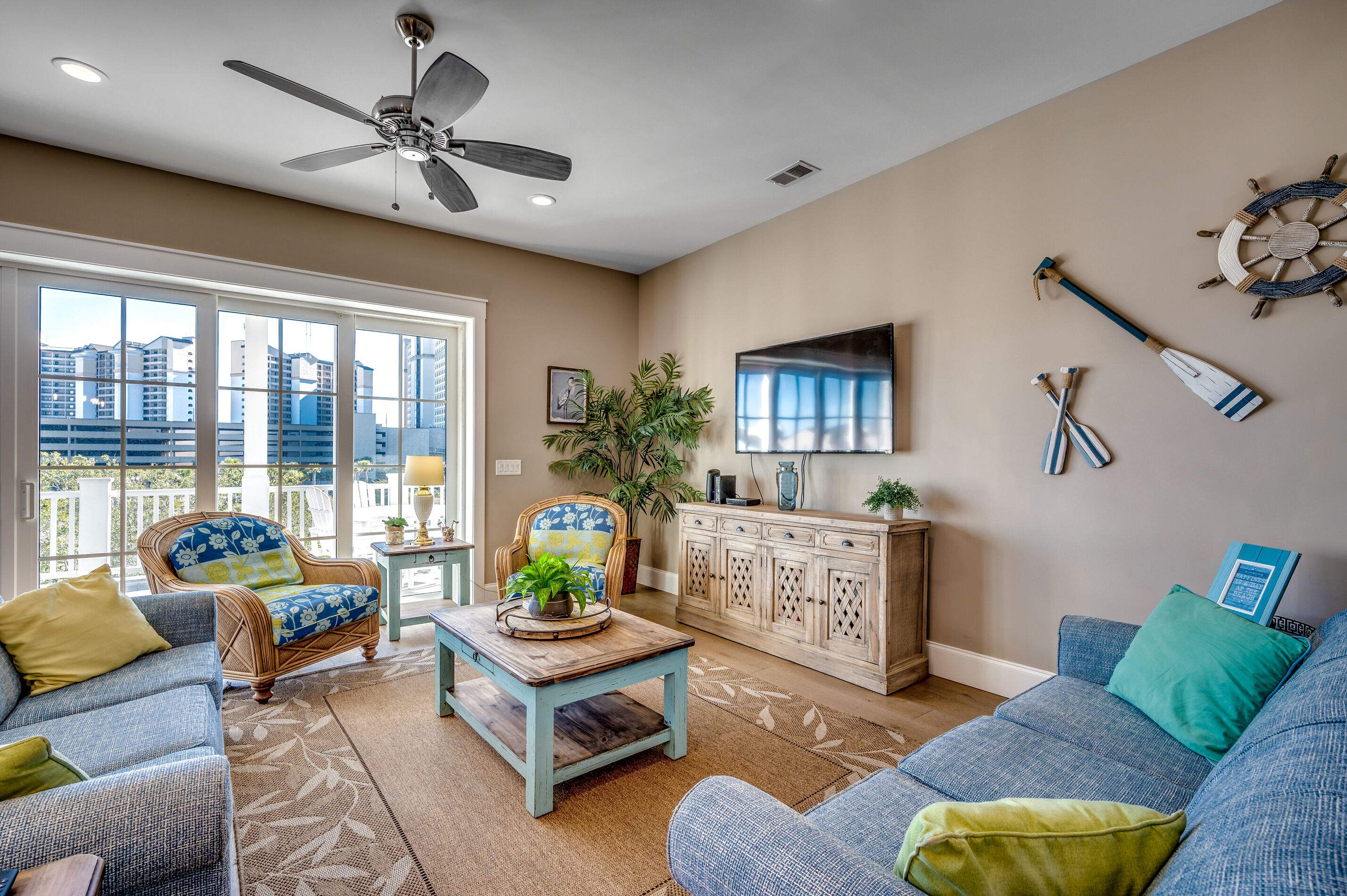 A spacious living room with a ceiling fan, large windows, a blue sofa, a coffee table, and a cabinet.