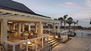 Ein Außenbereich mit Terrasse, Tischen, Stühlen, einem Pool und Palmen.