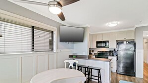 Eine moderne Küche mit Kochinsel, Deckenventilator und einem flachbildfernseher, der über der Insel angebracht ist.