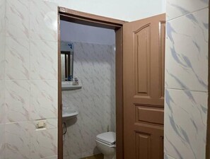 Un baño con baldosas de mármol blanco, un inodoro blanco, un espejo sobre el lavabo y una puerta de madera.