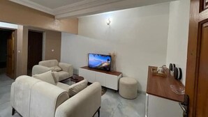 Ein modernes Wohnzimmer mit einer Sofagarnitur, einem Couchtisch, einem Fernseher und einem kleinen Holznachttisch.
