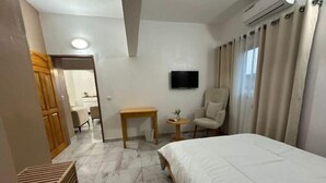 Ein Hotelzimmer mit Bett, Wandfernseher, Sessel, kleinem Tisch und einer Holzbank.
